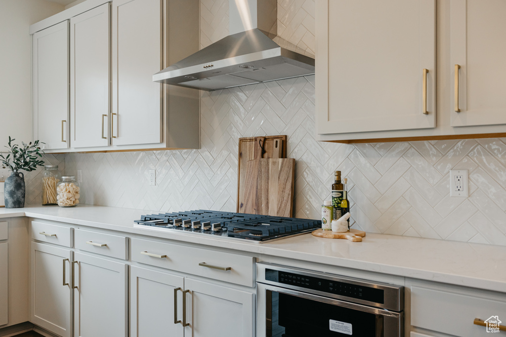Kitchen featuring wall chimney range hood, stainless steel appliances, tasteful backsplash, and light stone countertops