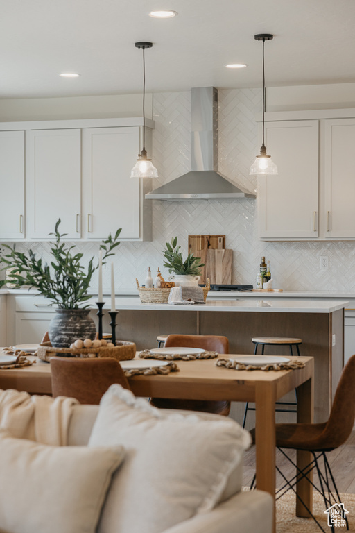 Kitchen featuring wall chimney range hood, decorative light fixtures, decorative backsplash, white cabinets, and recessed lighting
