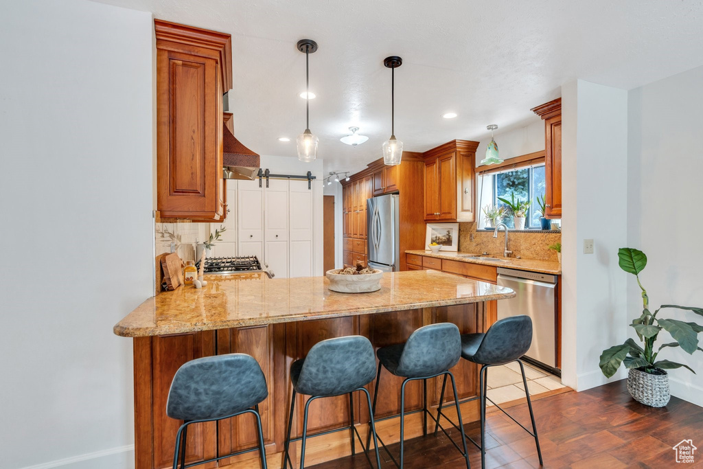 Kitchen featuring appliances with stainless steel finishes, decorative backsplash, a peninsula, light stone counters, and recessed lighting