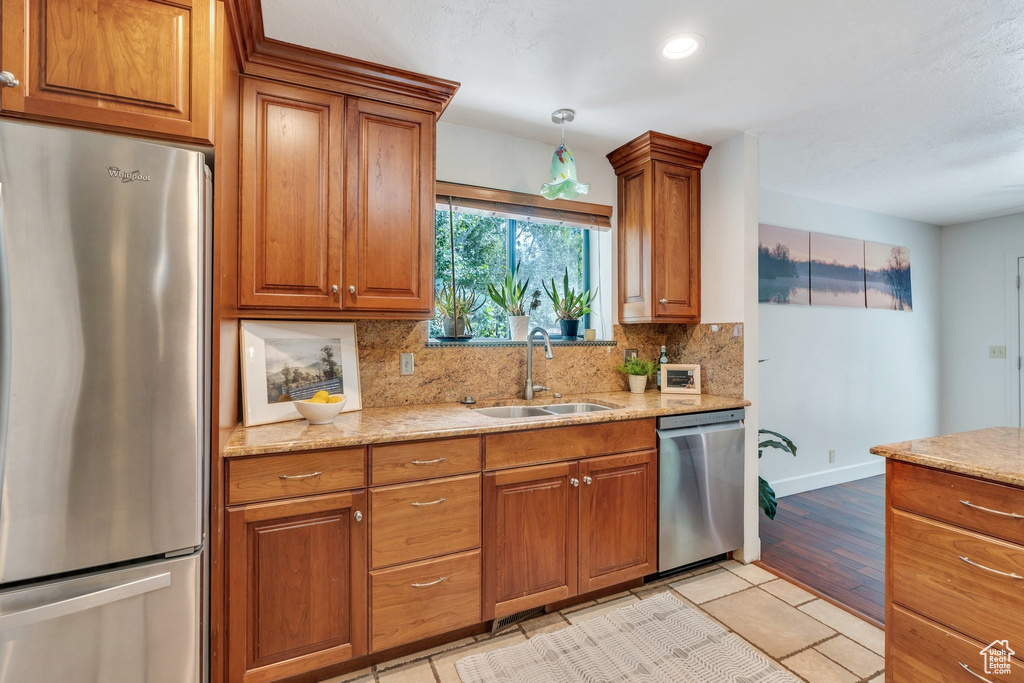 Kitchen featuring appliances with stainless steel finishes, tasteful backsplash, brown cabinetry, light stone counters, and recessed lighting