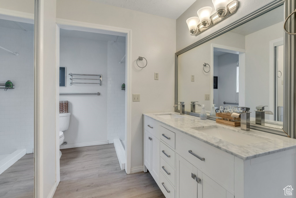 Bathroom featuring double vanity, wood finished floors, and tiled shower