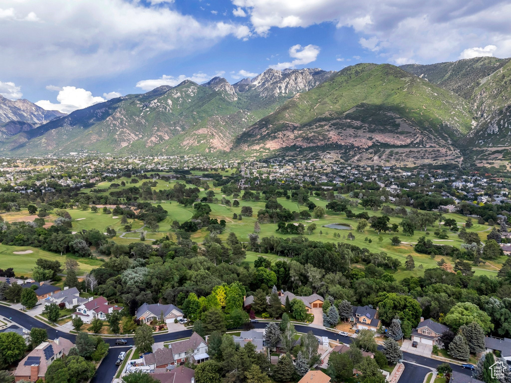 Aerial view of property and surrounding area with a golf course, a mountain backdrop, and nearby suburban area