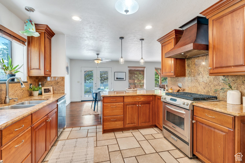 Kitchen featuring appliances with stainless steel finishes, custom exhaust hood, a peninsula, brown cabinets, and recessed lighting