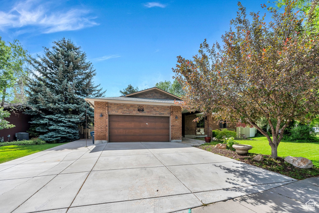 View of front of house with a garage, driveway, brick siding, and a front yard