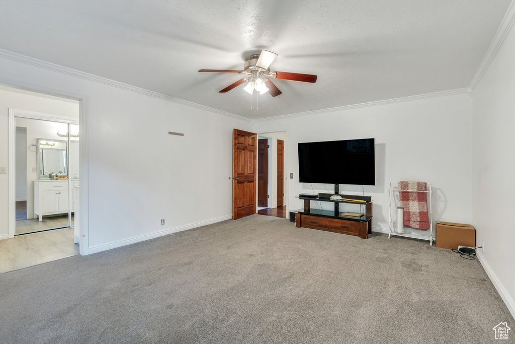 Unfurnished living room with a ceiling fan, ornamental molding, and carpet floors