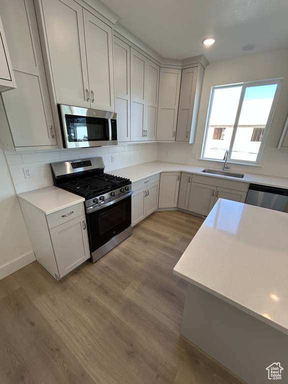 Kitchen with stainless steel appliances, light wood-style flooring, tasteful backsplash, light countertops, and recessed lighting