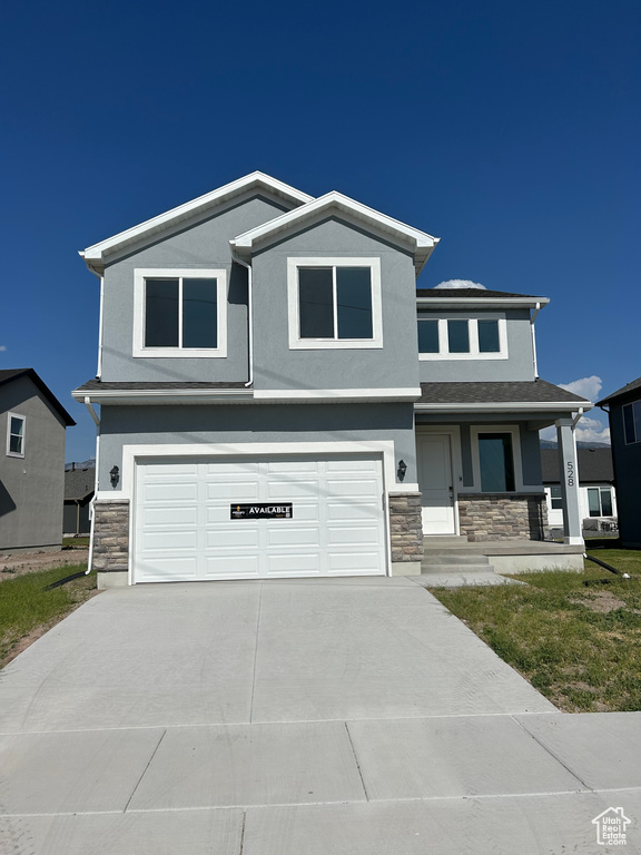 View of front facade with stone siding, an attached garage, and stucco siding