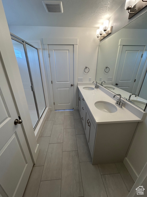 Bathroom with a shower stall, double vanity, and a textured ceiling