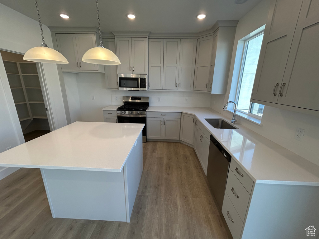 Kitchen with appliances with stainless steel finishes, light wood-type flooring, a kitchen island, recessed lighting, and hanging light fixtures