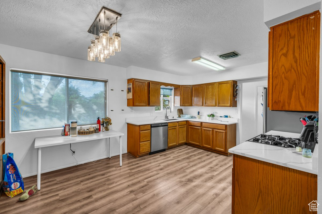 Kitchen with stainless steel appliances, brown cabinetry, a textured ceiling, light wood-style flooring, and a chandelier