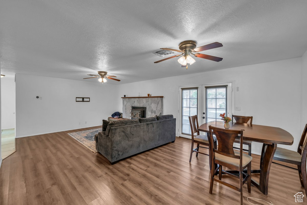 Living room with ceiling fan, a textured ceiling, a stone fireplace, and wood finished floors