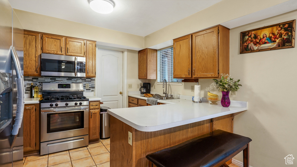 Kitchen with stainless steel appliances, brown cabinets, light countertops, and backsplash