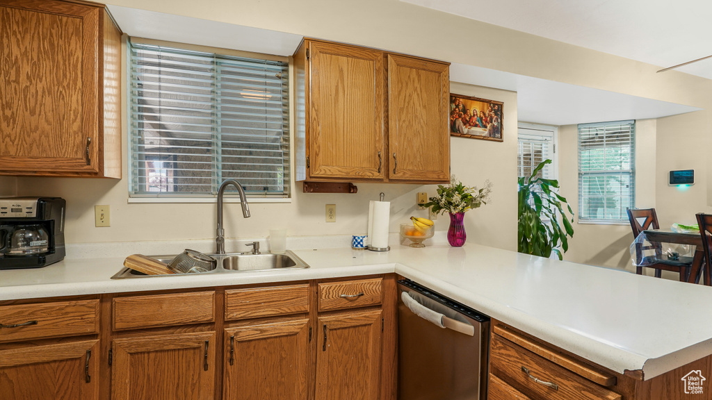 Kitchen featuring stainless steel dishwasher, a peninsula, light countertops, and brown cabinets