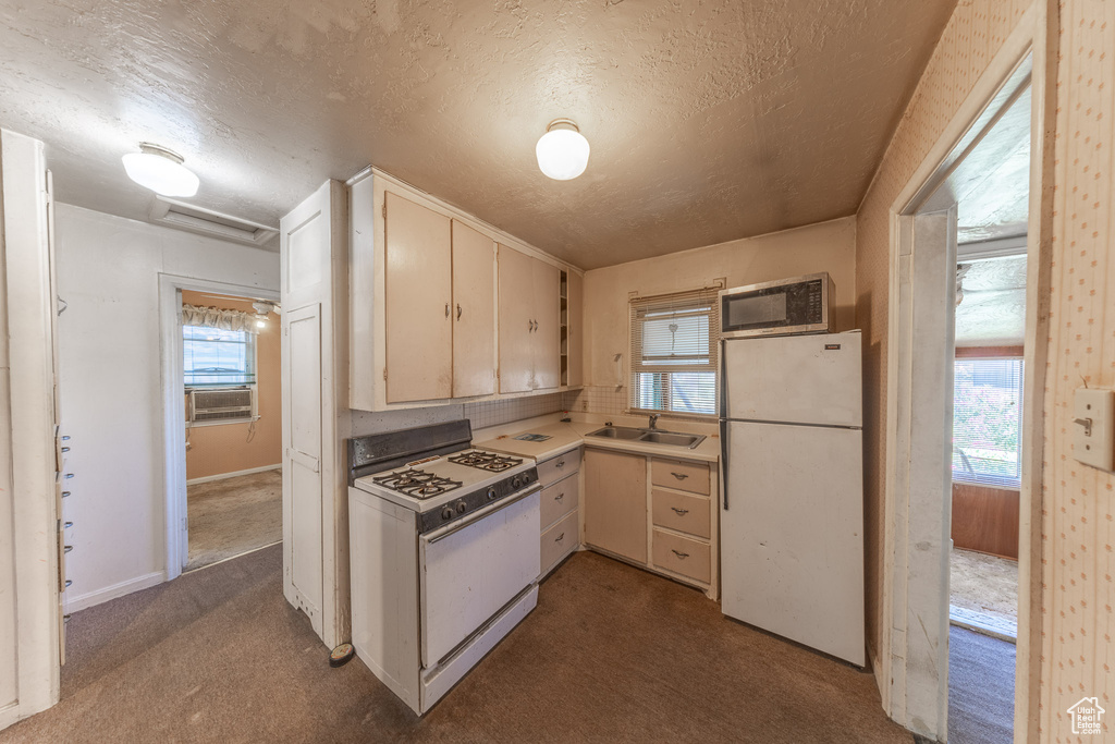 Kitchen featuring white appliances, carpet flooring, a textured ceiling, plenty of natural light, and cooling unit