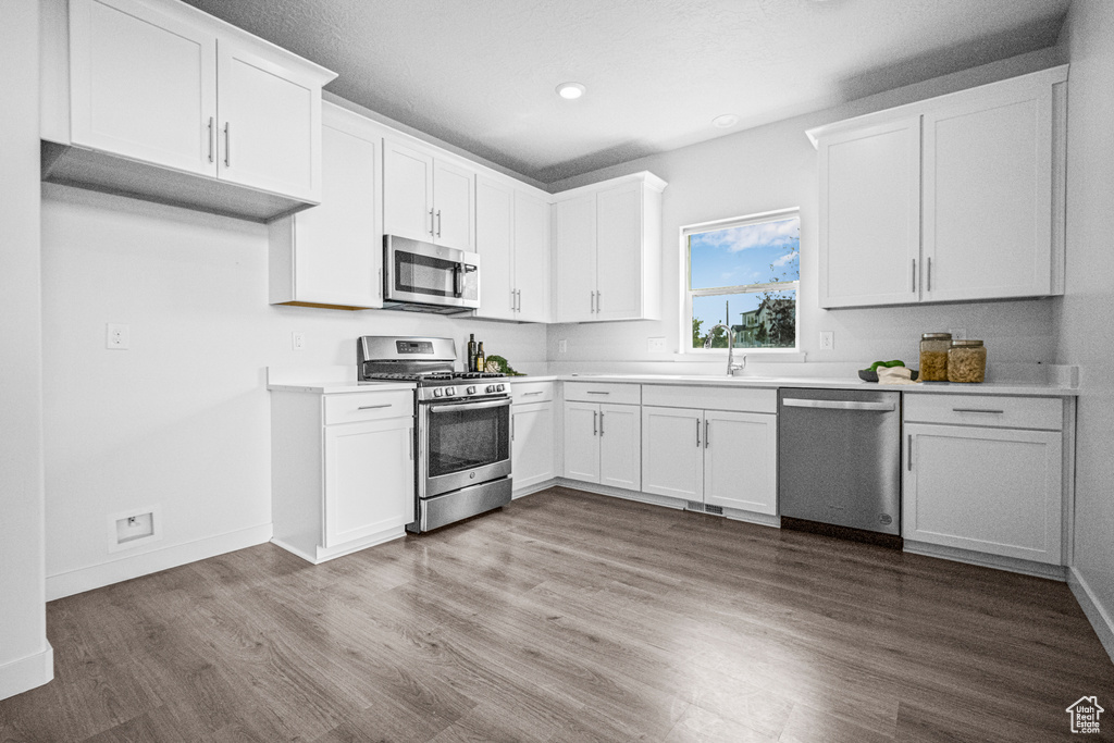 Kitchen featuring stainless steel appliances, wood finished floors, white cabinets, light countertops, and recessed lighting