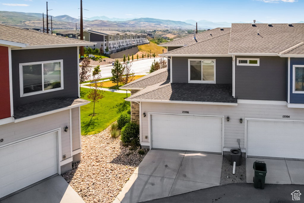View of front facade featuring a mountain view, roof with shingles, driveway, and an attached garage