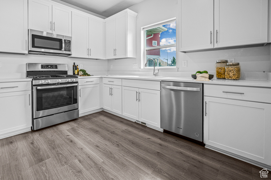 Kitchen featuring appliances with stainless steel finishes, light countertops, wood finished floors, and white cabinetry