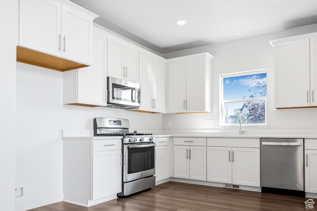 Kitchen featuring stainless steel appliances, dark wood-style floors, light countertops, white cabinetry, and recessed lighting