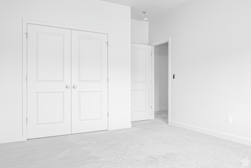 Unfurnished bedroom with a closet, light colored carpet, and baseboards