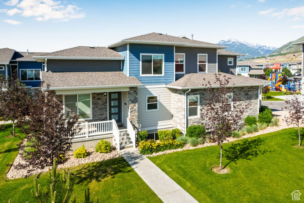 Prairie-style home featuring a porch, a front yard, a mountain view, stone siding, and a shingled roof