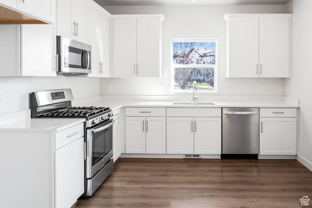 Kitchen with appliances with stainless steel finishes, a sink, dark wood finished floors, and white cabinetry