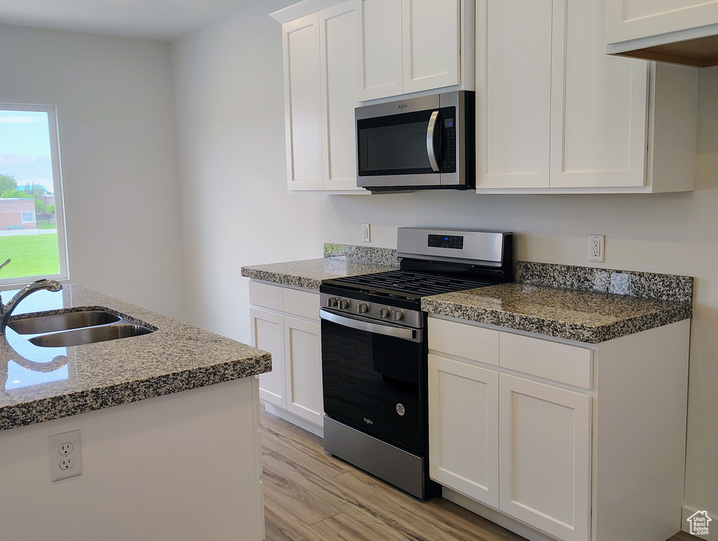 Kitchen featuring stainless steel appliances, light wood-type flooring, white cabinets, and dark stone countertops