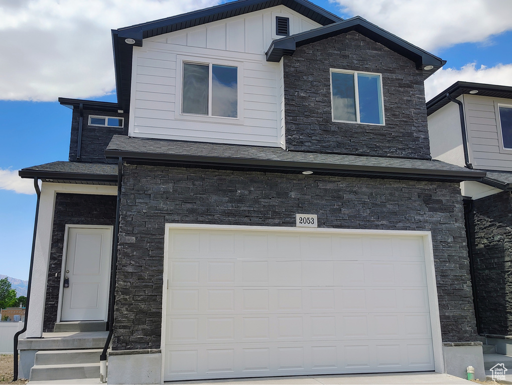 View of front of home with an attached garage, stone siding, and board and batten siding