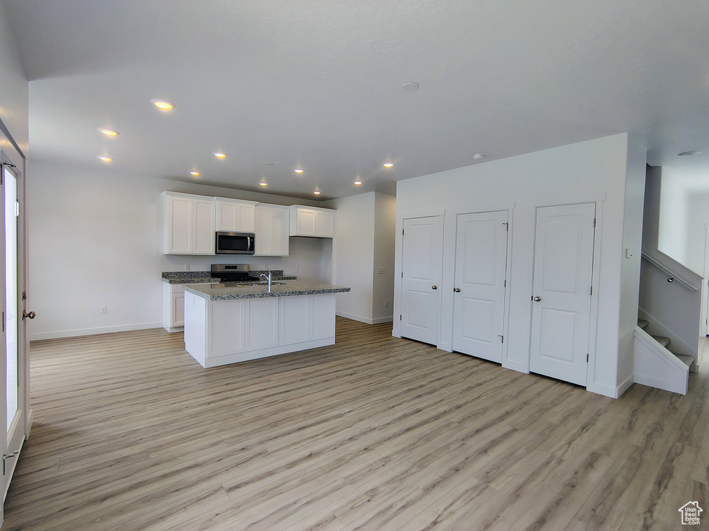Kitchen featuring stainless steel microwave, range, light wood-style floors, white cabinetry, and a kitchen island with sink