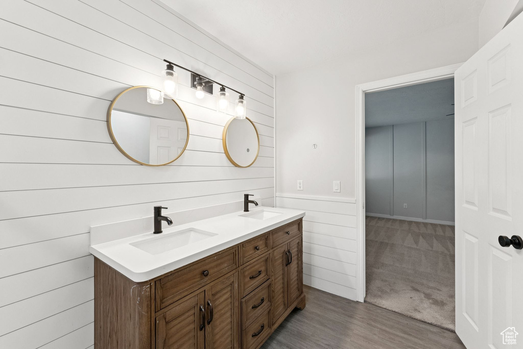 Full bath with wood walls, double vanity, and wood finished floors