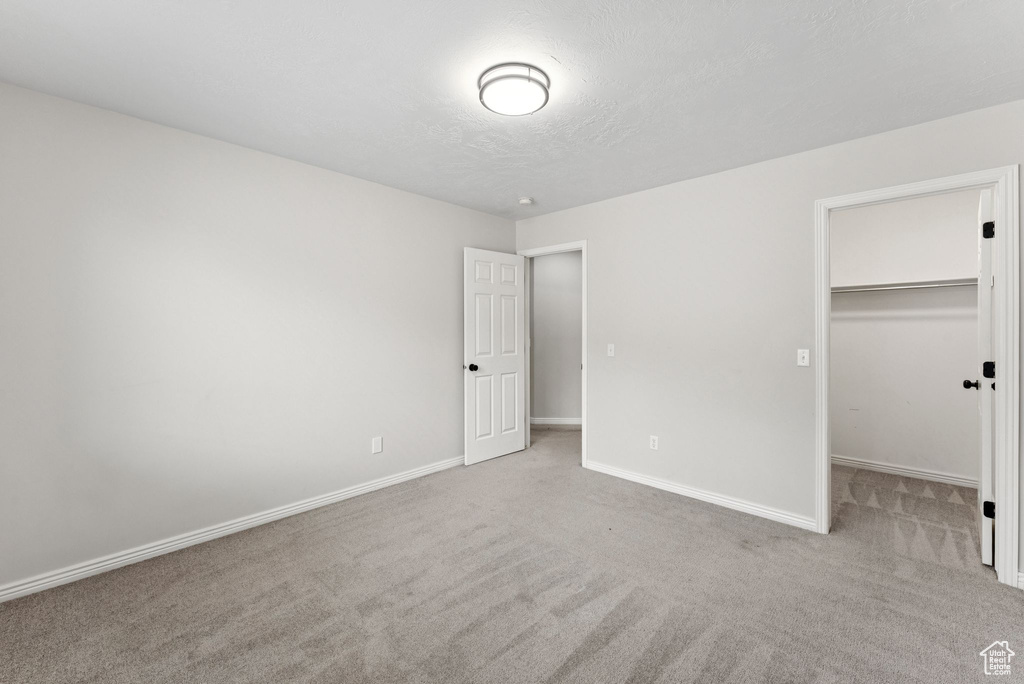 Unfurnished bedroom featuring carpet floors, a walk in closet, a textured ceiling, and a closet