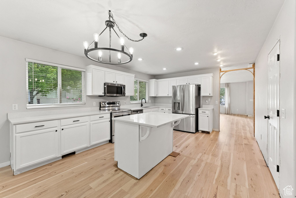 Kitchen featuring stainless steel appliances, light wood-style floors, white cabinets, light countertops, and a chandelier
