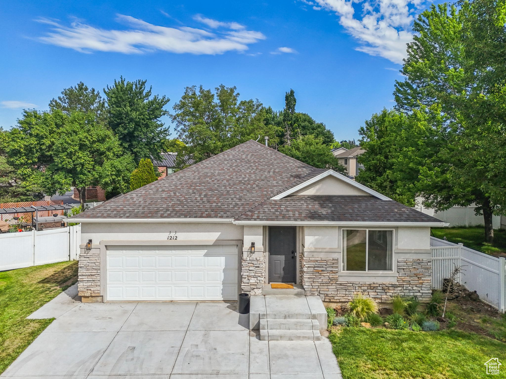 Ranch-style house featuring an attached garage, a shingled roof, driveway, and stone siding