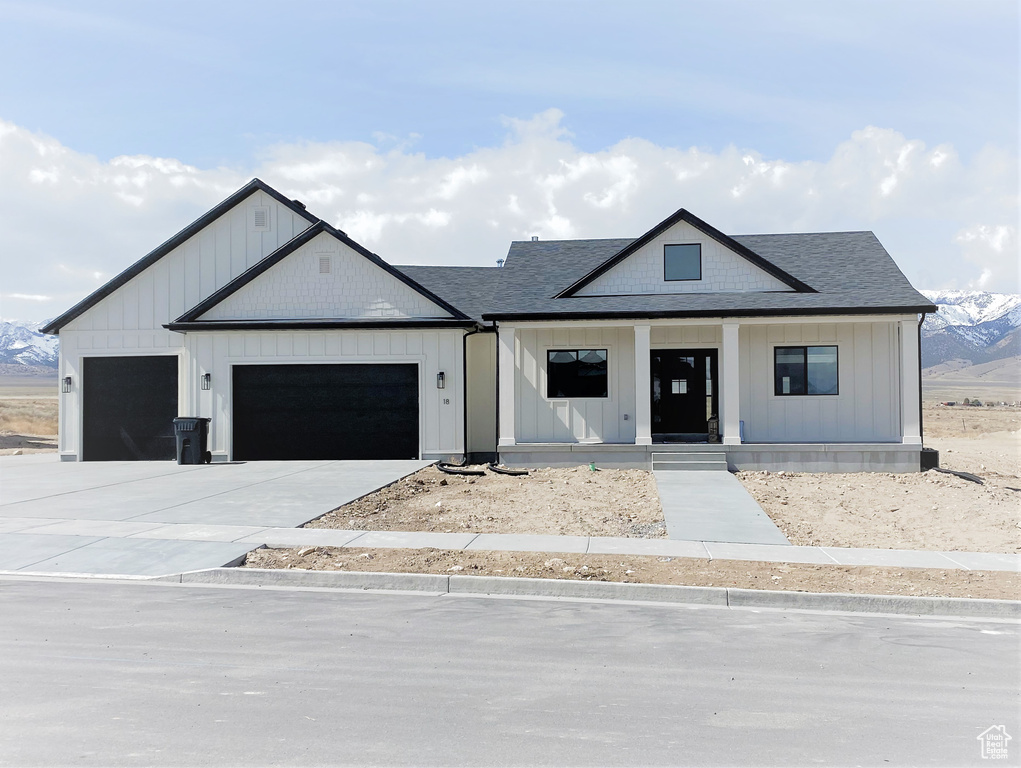 Modern inspired farmhouse featuring an attached garage, covered porch, board and batten siding, a shingled roof, and driveway