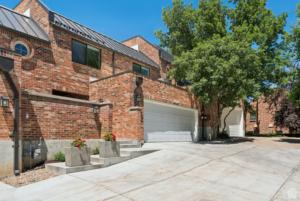 View of front of property with a standing seam roof, a garage, driveway, brick siding, and a metal roof