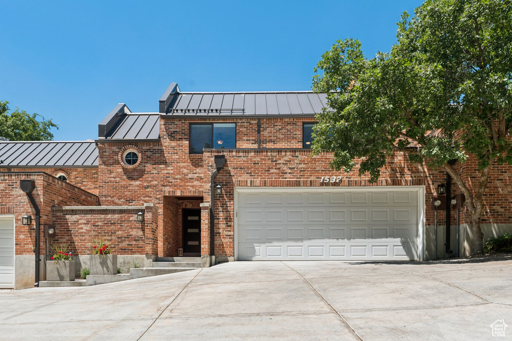 Front of property with a standing seam roof, concrete driveway, brick siding, a metal roof, and an attached garage