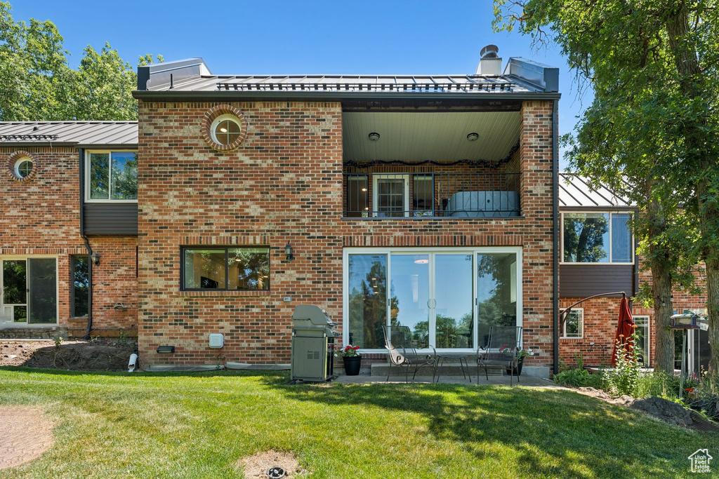 Rear view of property with a standing seam roof, a balcony, a yard, brick siding, and a patio