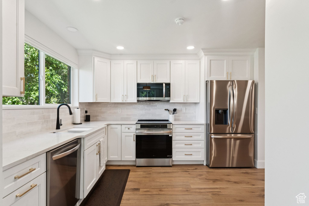 Kitchen featuring appliances with stainless steel finishes, decorative backsplash, white cabinets, light wood-type flooring, and recessed lighting