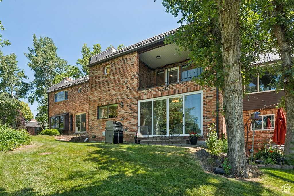 Back of property featuring a balcony, a yard, and brick siding