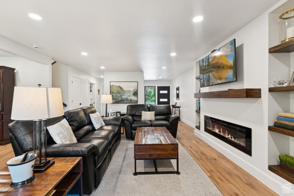 Living room with light wood finished floors, recessed lighting, and a glass covered fireplace