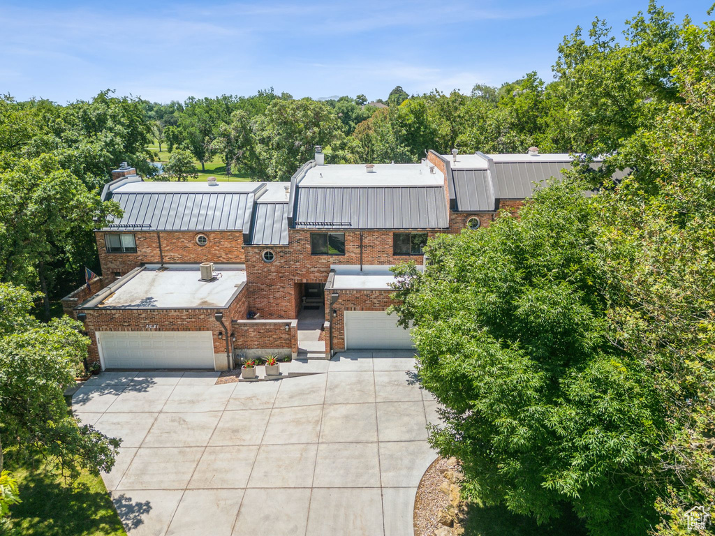 View of front of home with driveway, a chimney, brick siding, an attached garage, and a metal roof