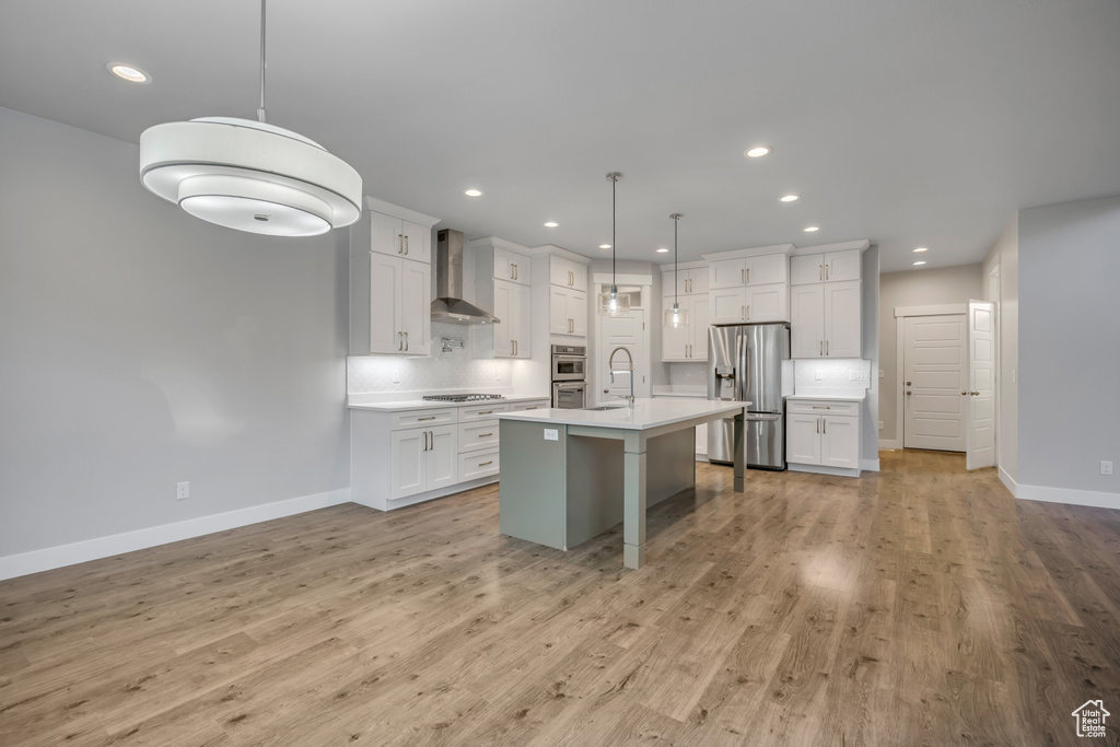 Kitchen with stainless steel appliances, wall chimney range hood, light countertops, tasteful backsplash, and white cabinets