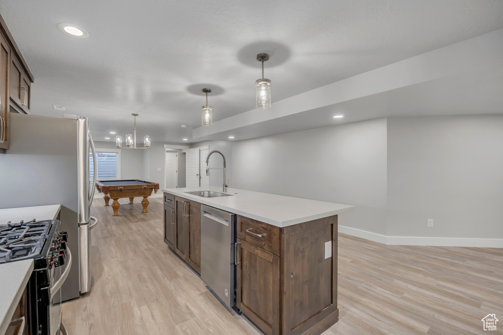 Kitchen featuring stainless steel appliances, light wood-style flooring, an island with sink, light countertops, and recessed lighting
