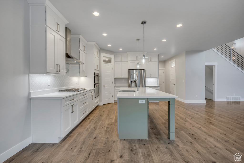 Kitchen featuring wall chimney range hood, appliances with stainless steel finishes, tasteful backsplash, light wood finished floors, and recessed lighting