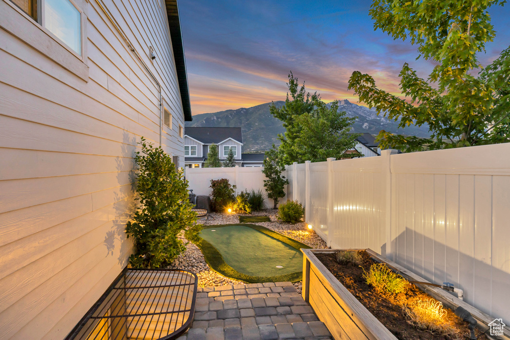 Patio terrace at dusk with a putting area, a fenced backyard, a mountain view, and a patio