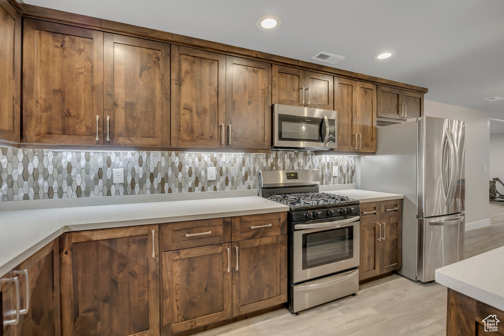 Kitchen with stainless steel appliances, tasteful backsplash, recessed lighting, light countertops, and light wood-type flooring