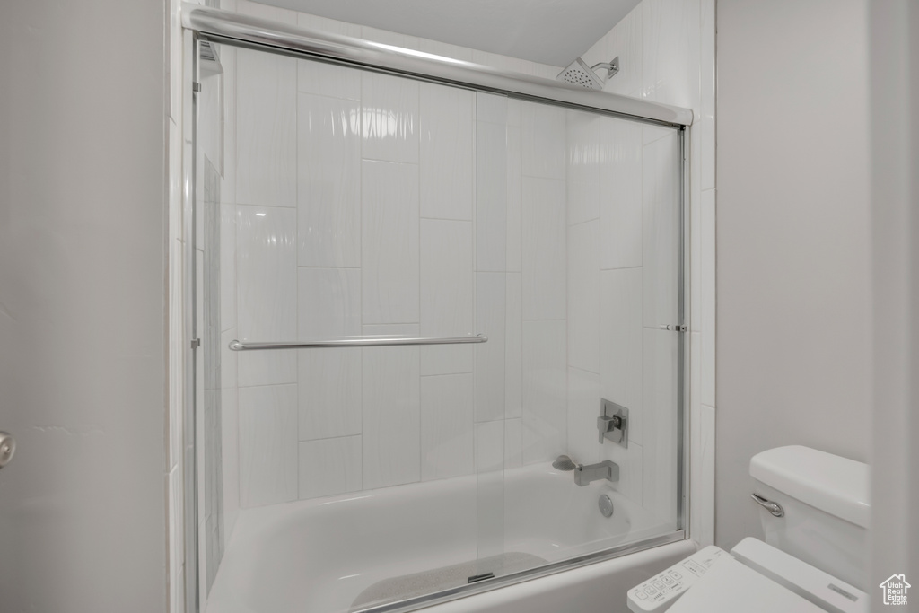 Bathroom featuring toilet and bath / shower combo with glass door
