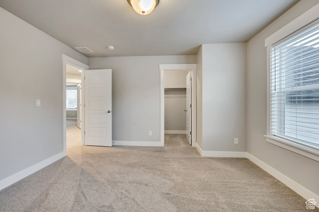 Unfurnished bedroom with light carpet, a walk in closet, and a closet