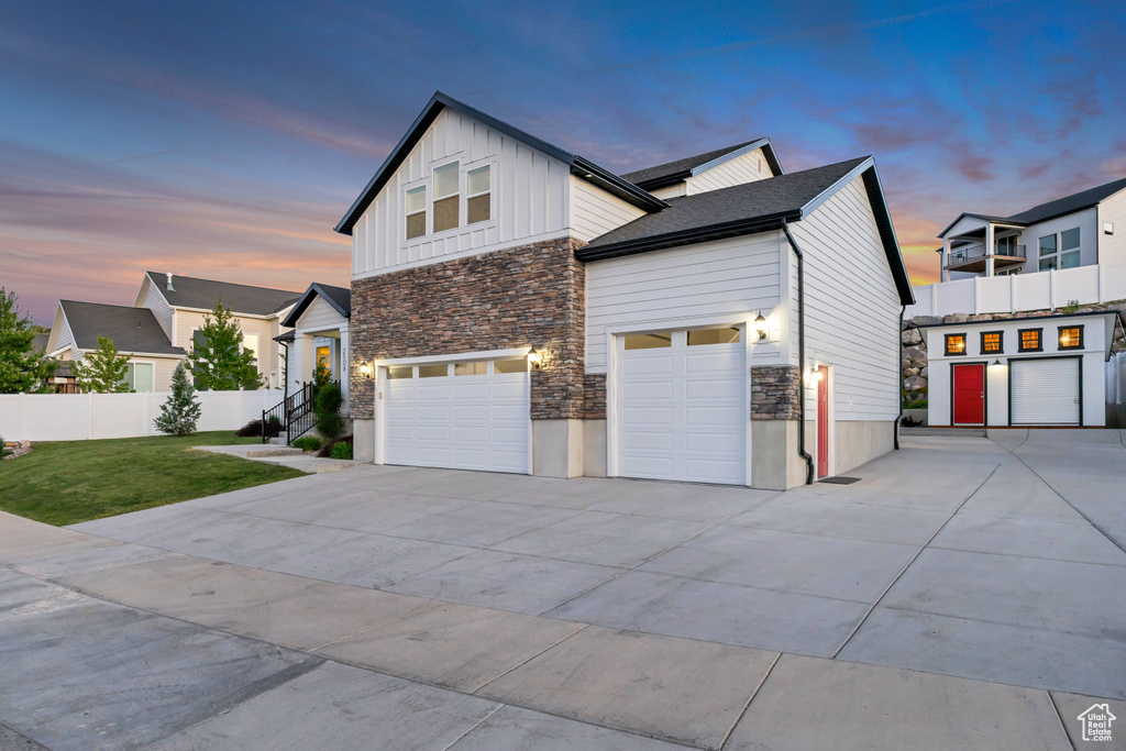 Property exterior at dusk featuring stone siding, driveway, board and batten siding, and an attached garage