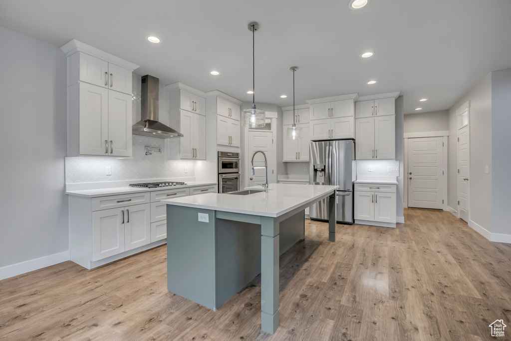 Kitchen featuring wall chimney exhaust hood, stainless steel appliances, white cabinets, tasteful backsplash, and light countertops