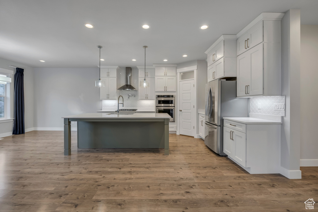Kitchen featuring wall chimney exhaust hood, appliances with stainless steel finishes, backsplash, a center island with sink, and recessed lighting